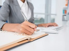 Imagem mostra uma mulher com uma caneta na mão escrevendo em um caderno