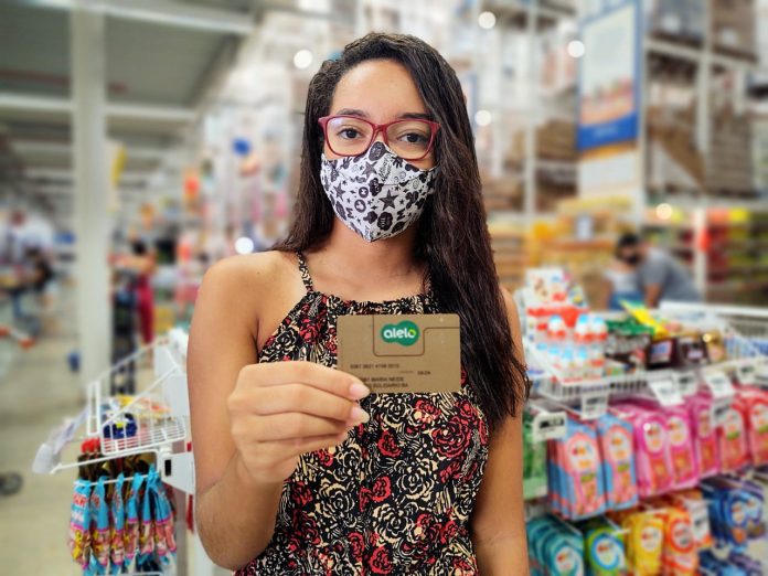 Estudante usando máscara mostra cartão bolsa presença dentro de um supermercado
