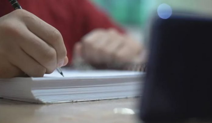 Foto desfocada mostra um estudante escrevendo em um caderno