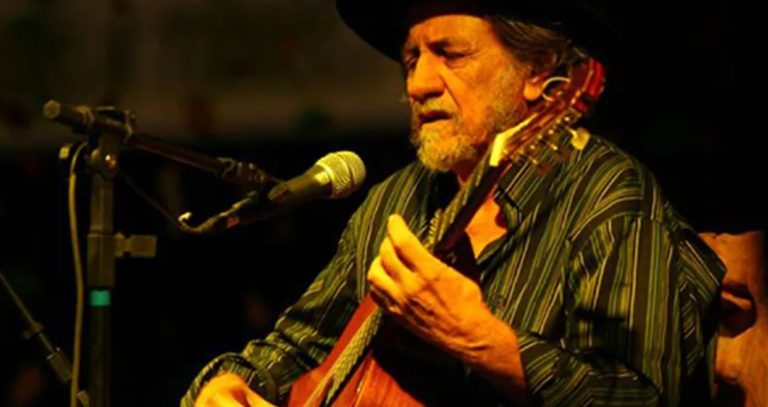 Foto mostra cantor Elomar tocando um violão em uma apresentação
