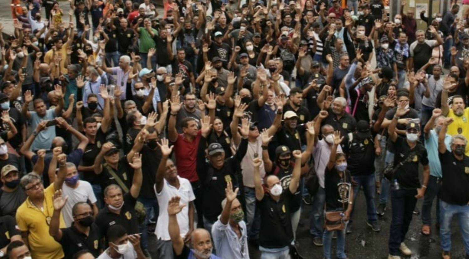 Foto mostra uma multidão de policiais civil de pé com as mão levantadas em uma assembleia em local aberto
