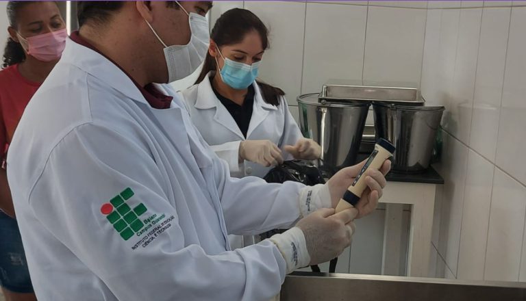 Foto mostro dois técnicos coletando amostra de água em um empreendimento onde trabalha uma mulher que também aparece na imagem
