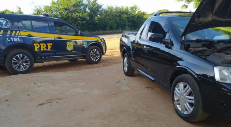 Foto mostra a lateral do veículo apreendido e a viatura da PRF ao fundo