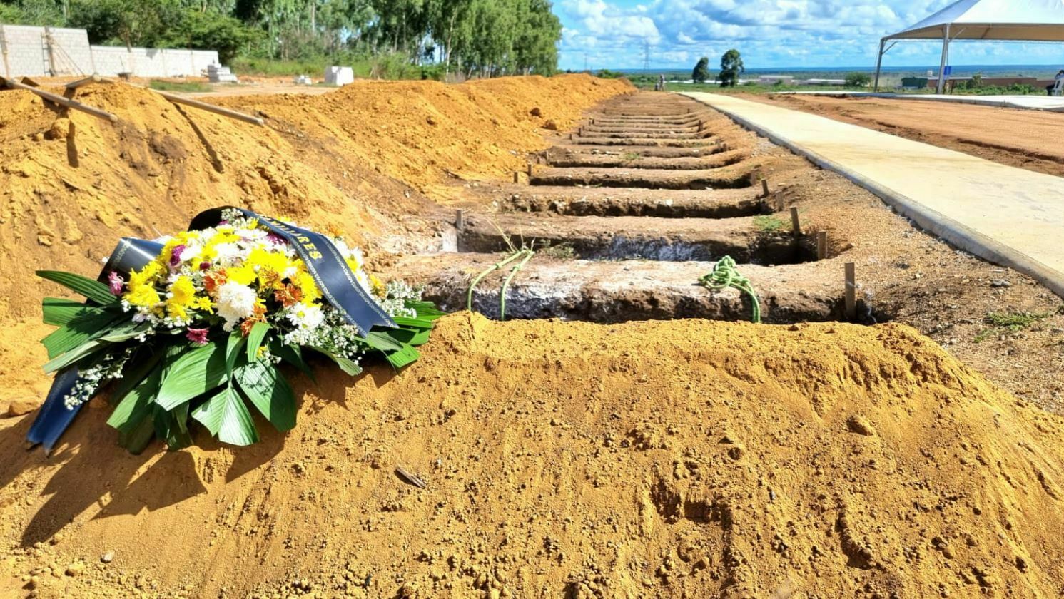 Imagem mostra uma coroa de flores na primeira cova usada para sepultamentos na cidade. Ao fundo, outras covas abertas