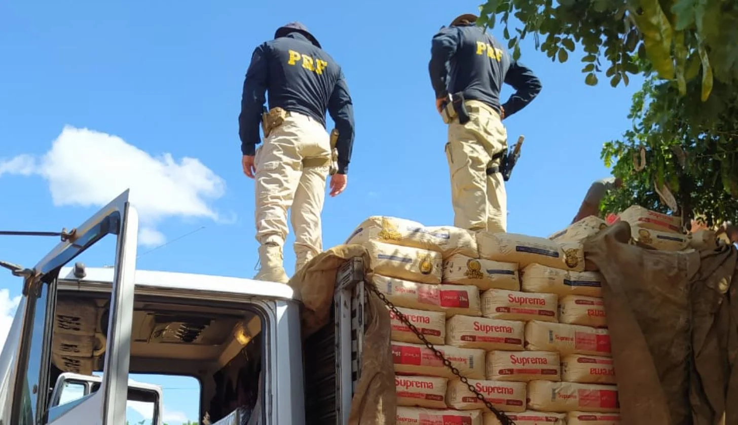 Foto mostra dois policiais rodoviários federais fazendo uma vistoria por cima da carga de farinha de trigo transportada no caminhão