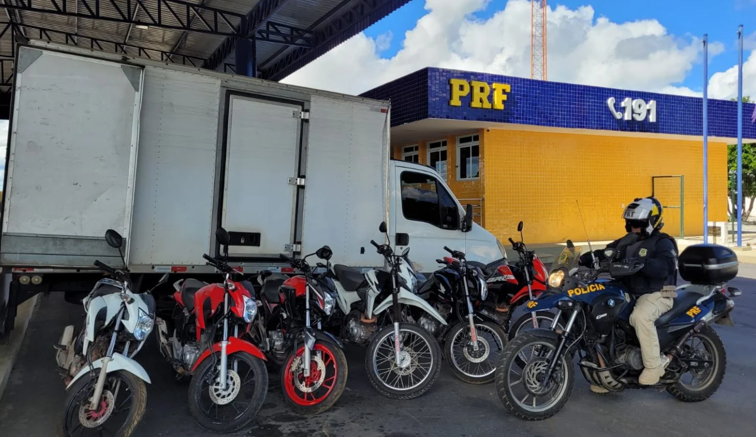 Foto mostra seis motos em frente ao caminhão baú e um policial em cima de uma motocicleta da PRF