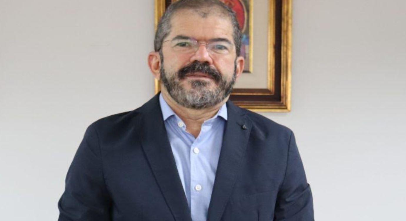 Foto mostra o presidente do Banco do Nordeste, um homem branco, usando óculos, com cabelos e barbas parcialmente grisalhos. ELe usa um terno preto e uma camisa azul clara.