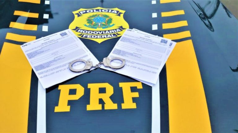 Foto mostra dois documentos e uma algema sobre o capô de uma viatura da PRF
