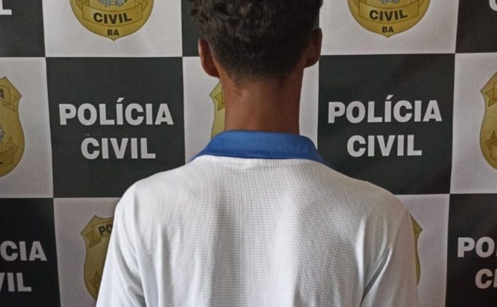 Imagem mostra acusado de violência doméstica de costas, de frente para um painel da polícia civil