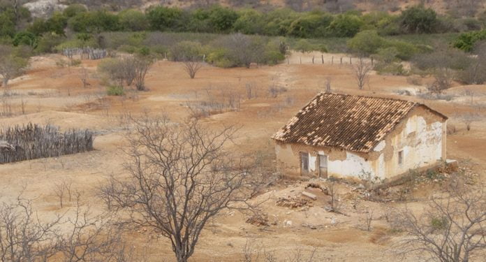 Foto mostra uma casa simples em meio a uma área com vegetação seca