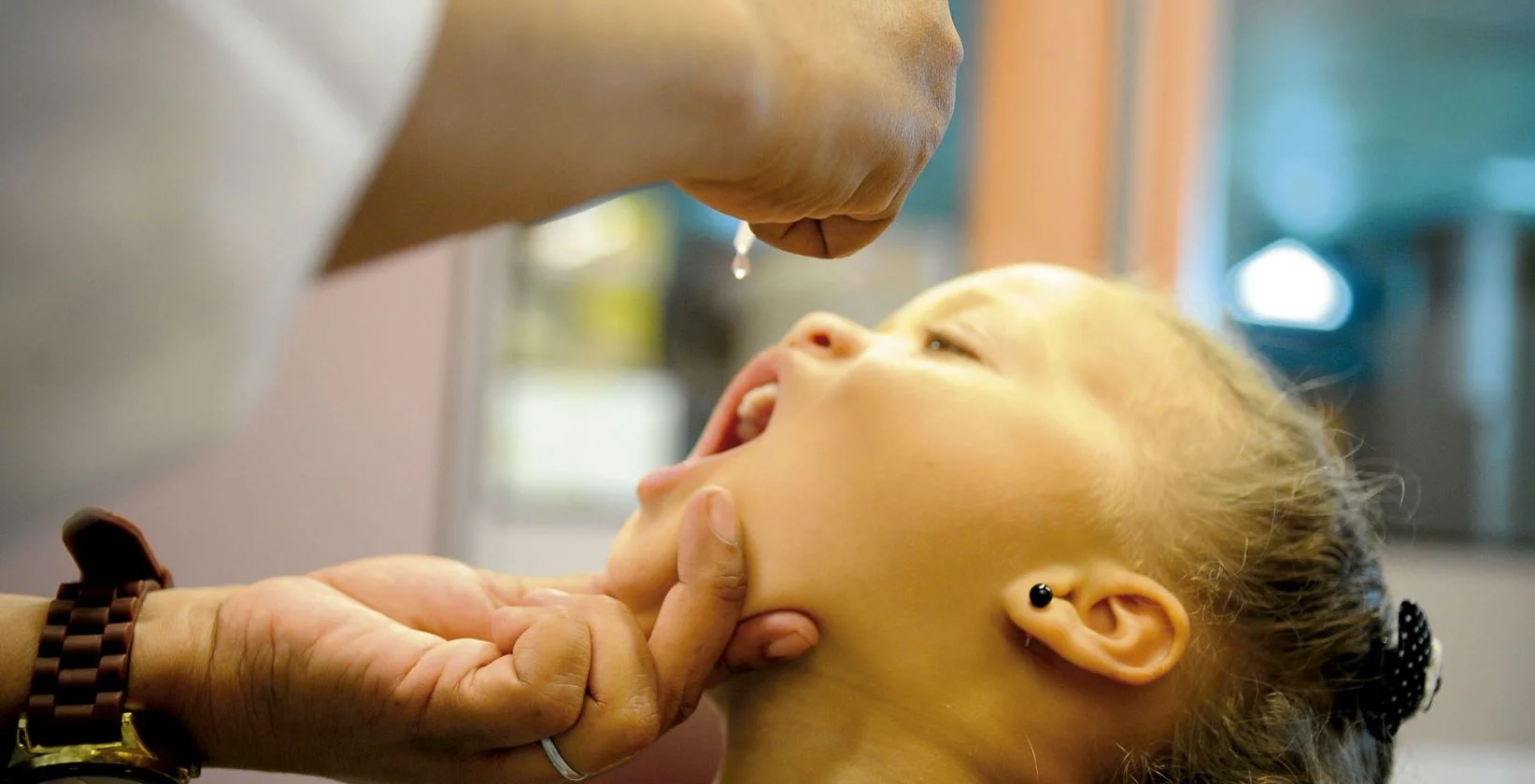 Foto mostra uma criança do sexo feminino recebendo uma vacina por via oral