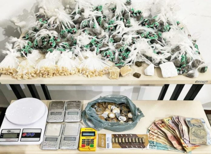Foto mostra as porções de drogas, balanças de precisão, munições, máquina de cartão e dinheiro
