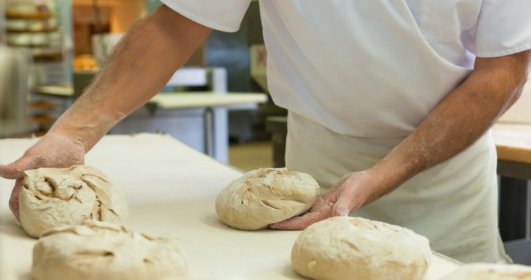 Foto mostra homem preparando massas de panificação sobre uma mesa