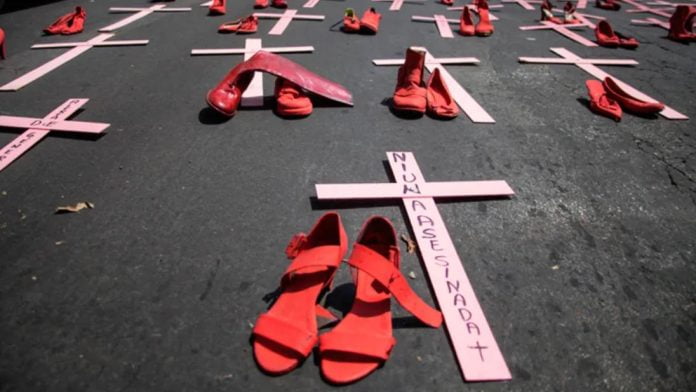 Foto mostra sandálias ao lado de cruzes sobre o chão simbolizando vítimas de feminicídio