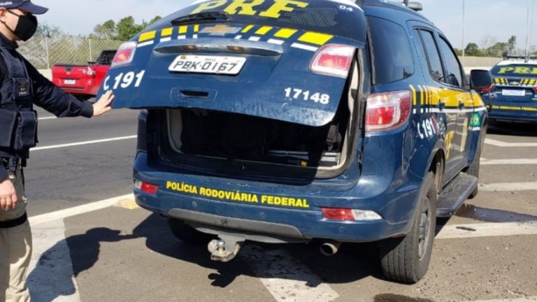Foto mostra um policial fechando o compartimento traseiro de uma viatura