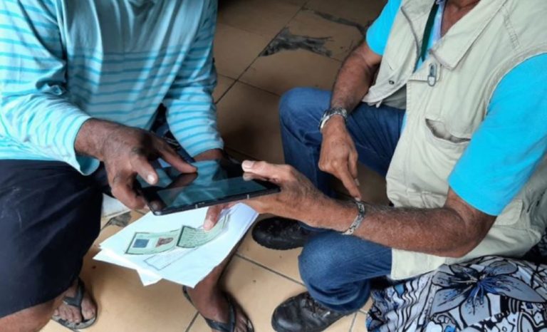 Foto mostra técnico do Incra mostrando um tablete e documentos a um assentado