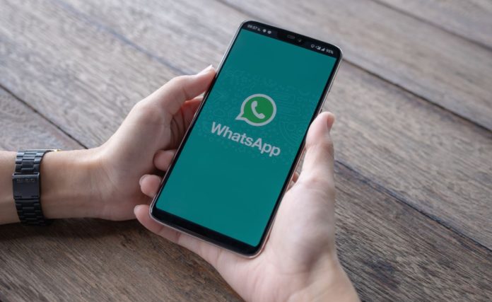 Foto mostra um celular sendo segurando por duas mãos sobre uma mesa de madeira - pacotão de melhorias do whatsapp