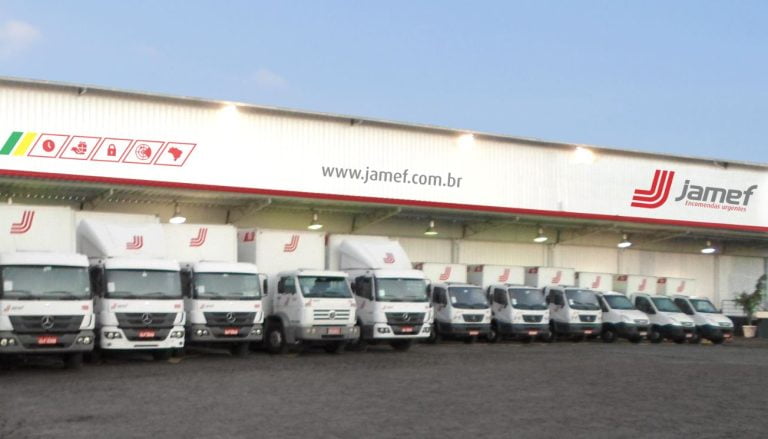 Foto mostra um galpão da empresa com vários caminhões estacionados em frente